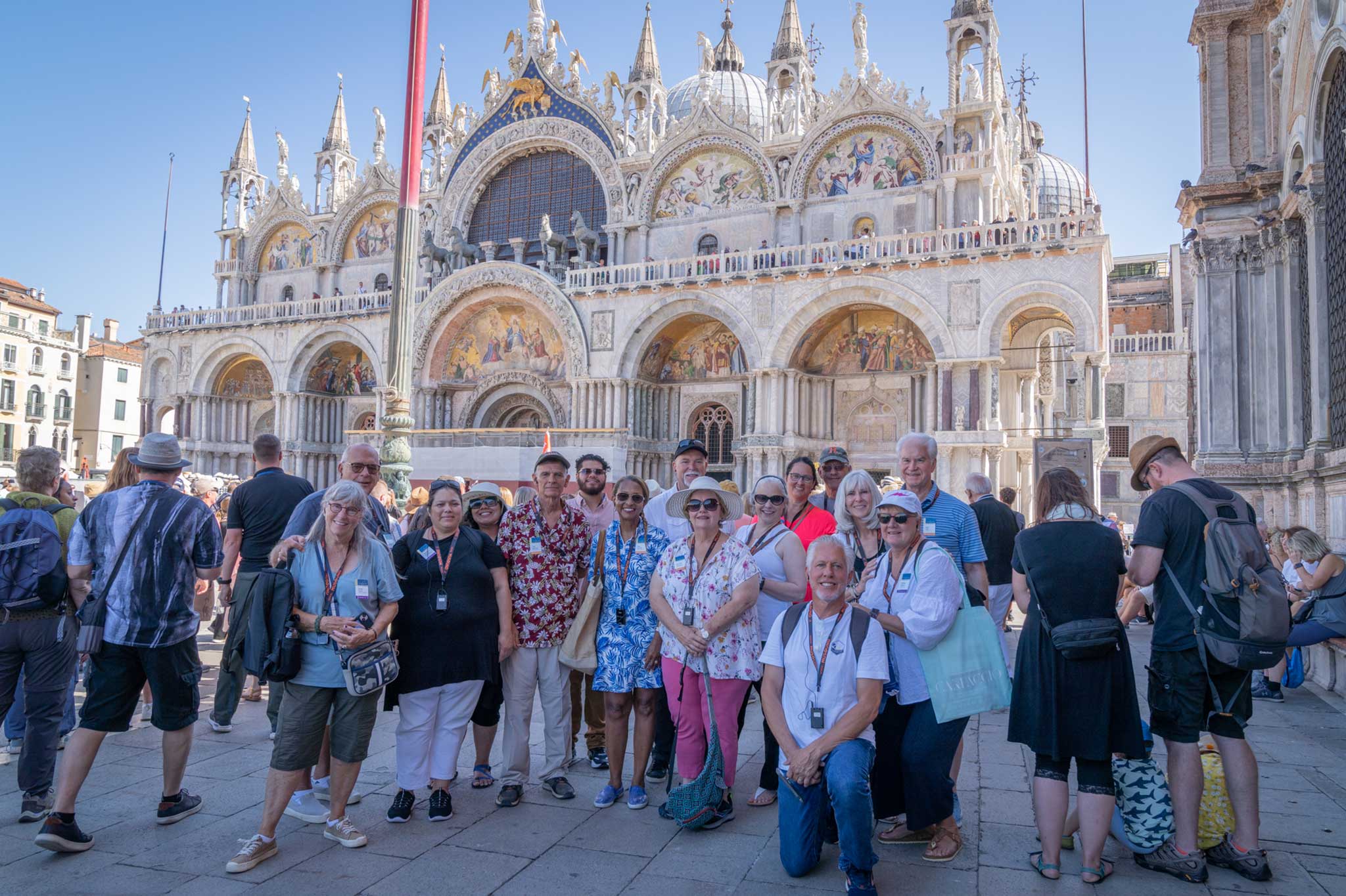 A group of travelers pose for the camera in the busy plaza of Saint Mark's Basilica church in Venice, Italy.