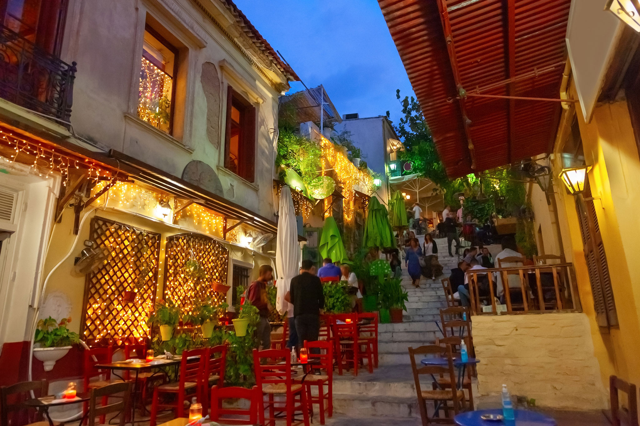 Lively atmosphere in the historic Plaka neighborhood of Athens with locals and tourists enjoying outdoor eateries among illuminated, colorful buildings.