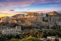 Historic ruins of the Acropolis in Athens during sunset with golden light casting shadows over the ancient structures and the city in the distance.