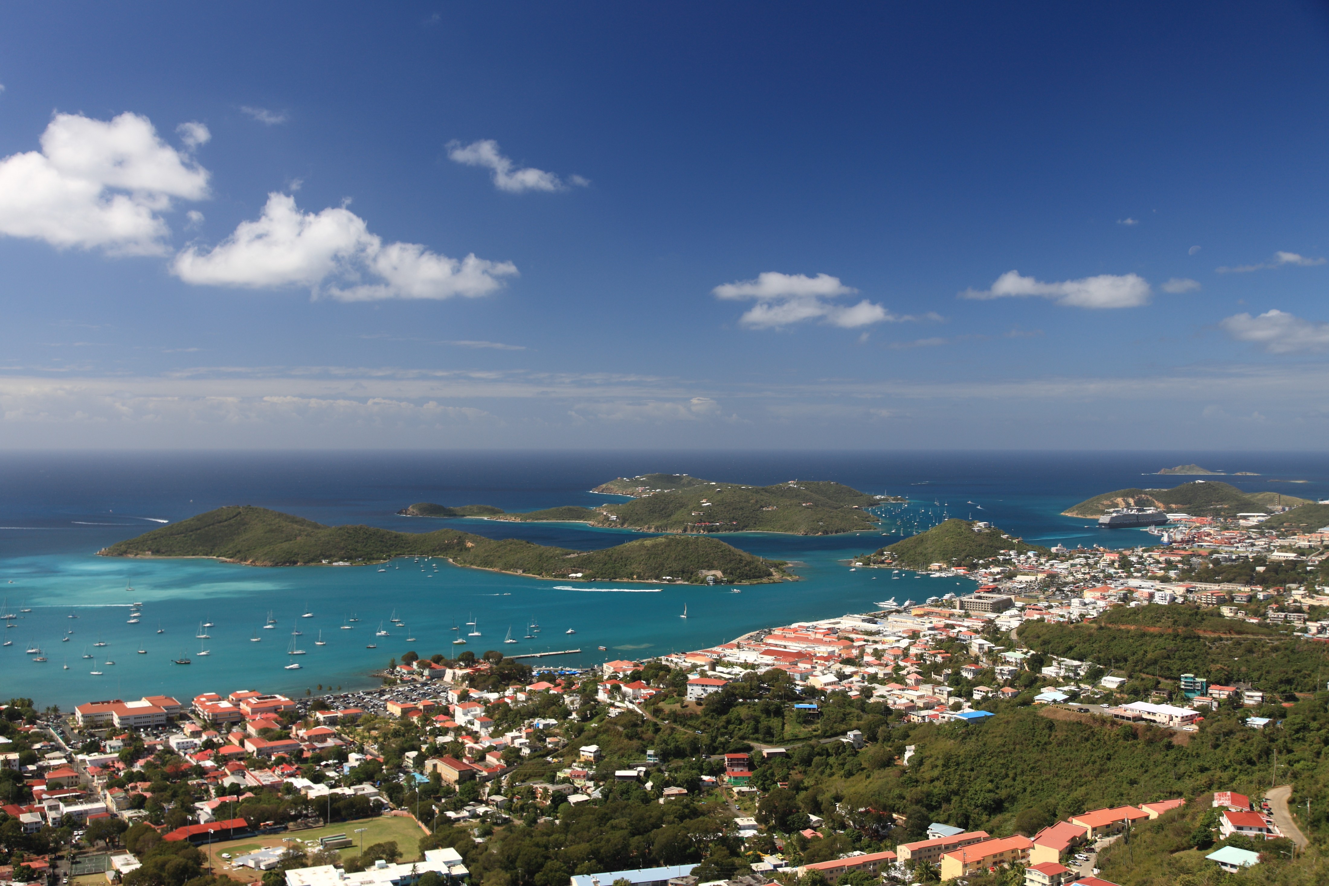 Wide, scenic view of St. Thomas island with boats, buildings, and green hills on a clear day