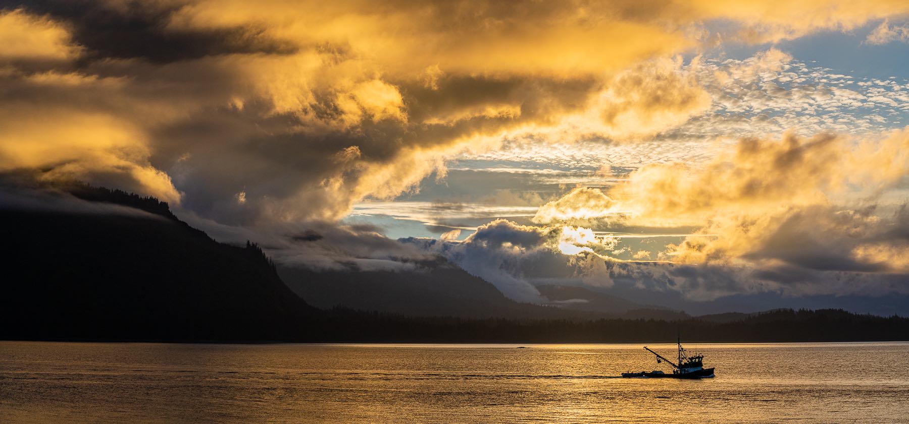 Panorama of a boat on the water with mountains and a golden sunset in the background