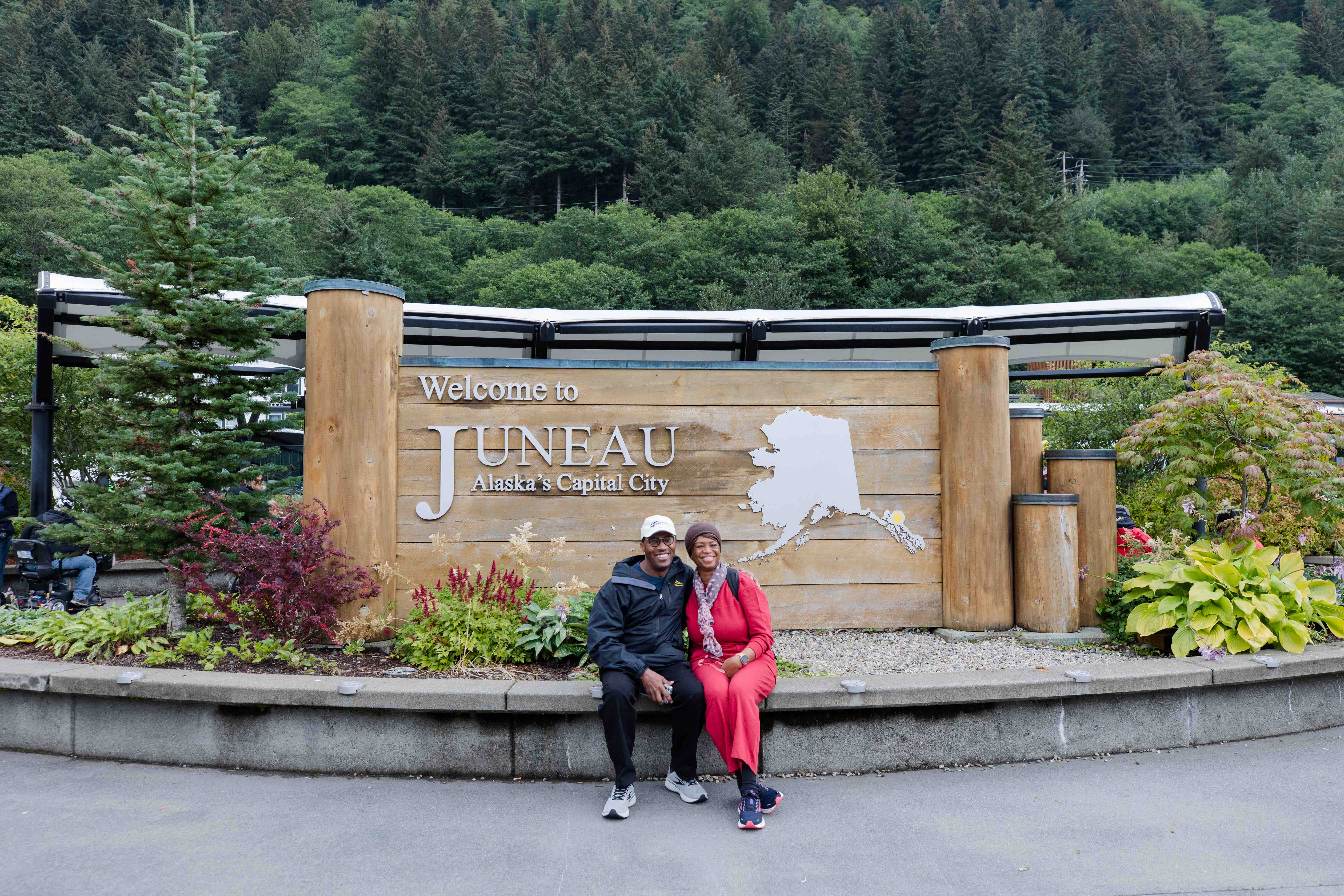 Inspiration travelers sitting in front of sign that says "Welcome to Juneau, Alaska's Capital City"