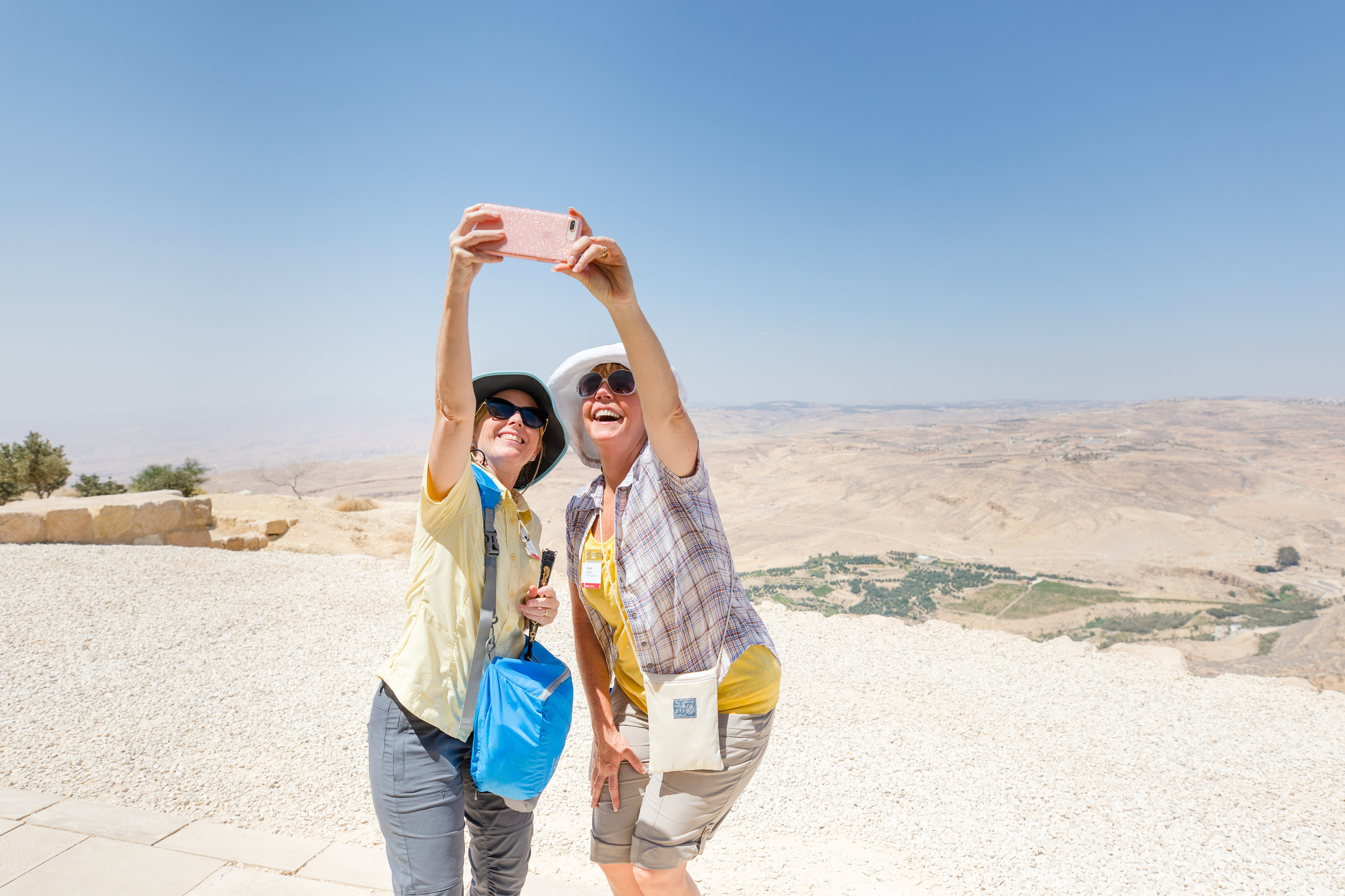 Two travelers hold an iPhone for a selfie on Mount Nebo