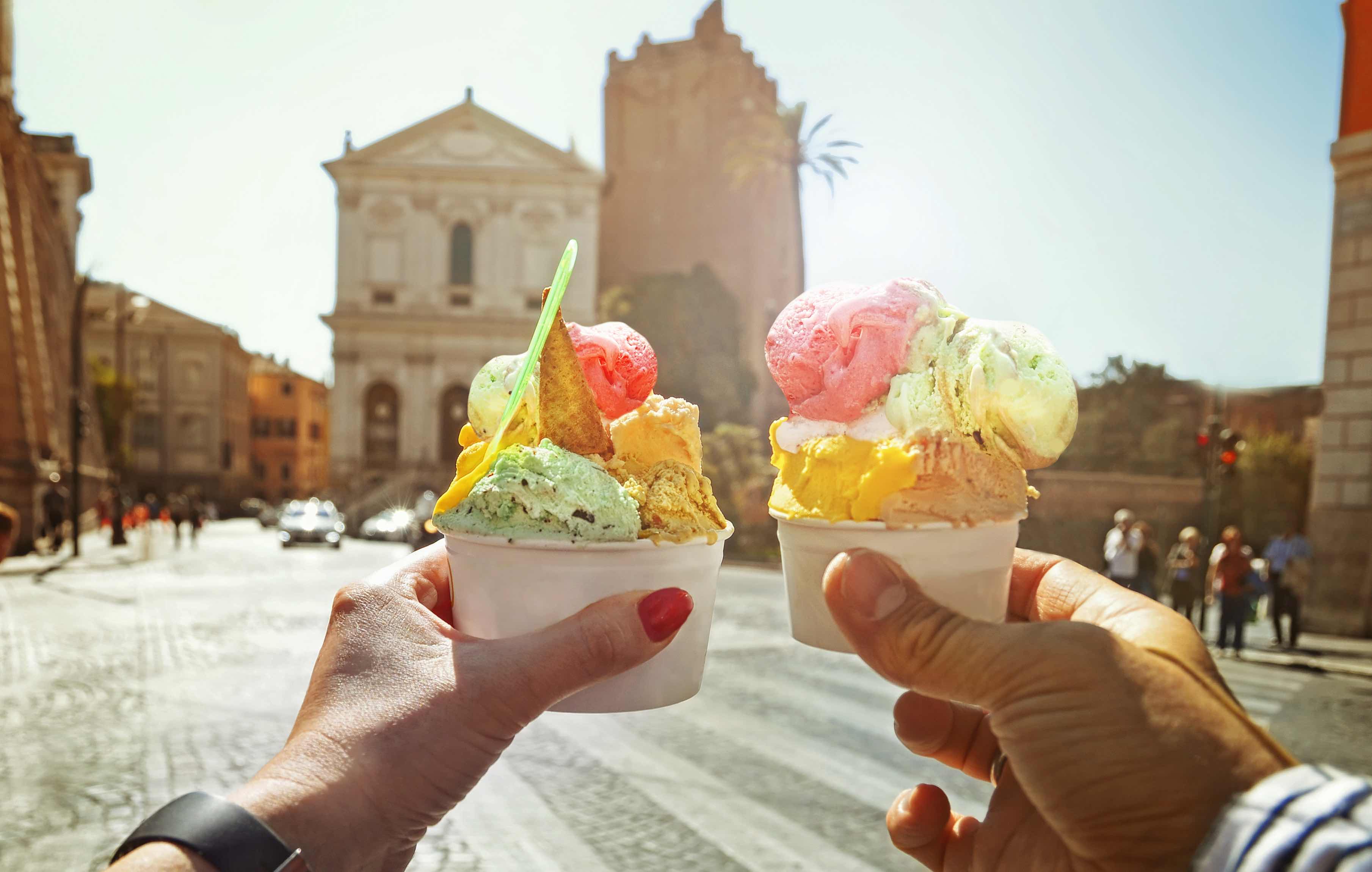 Couple with beautiful bright sweet Italian ice-cream with different flavors in their hands on the square in Rome, Italy